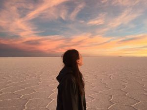 Vrouwelijke backpacker kijkt naar de ondergaande zon op de zoutvlakte van Uyuni in Bolivia
