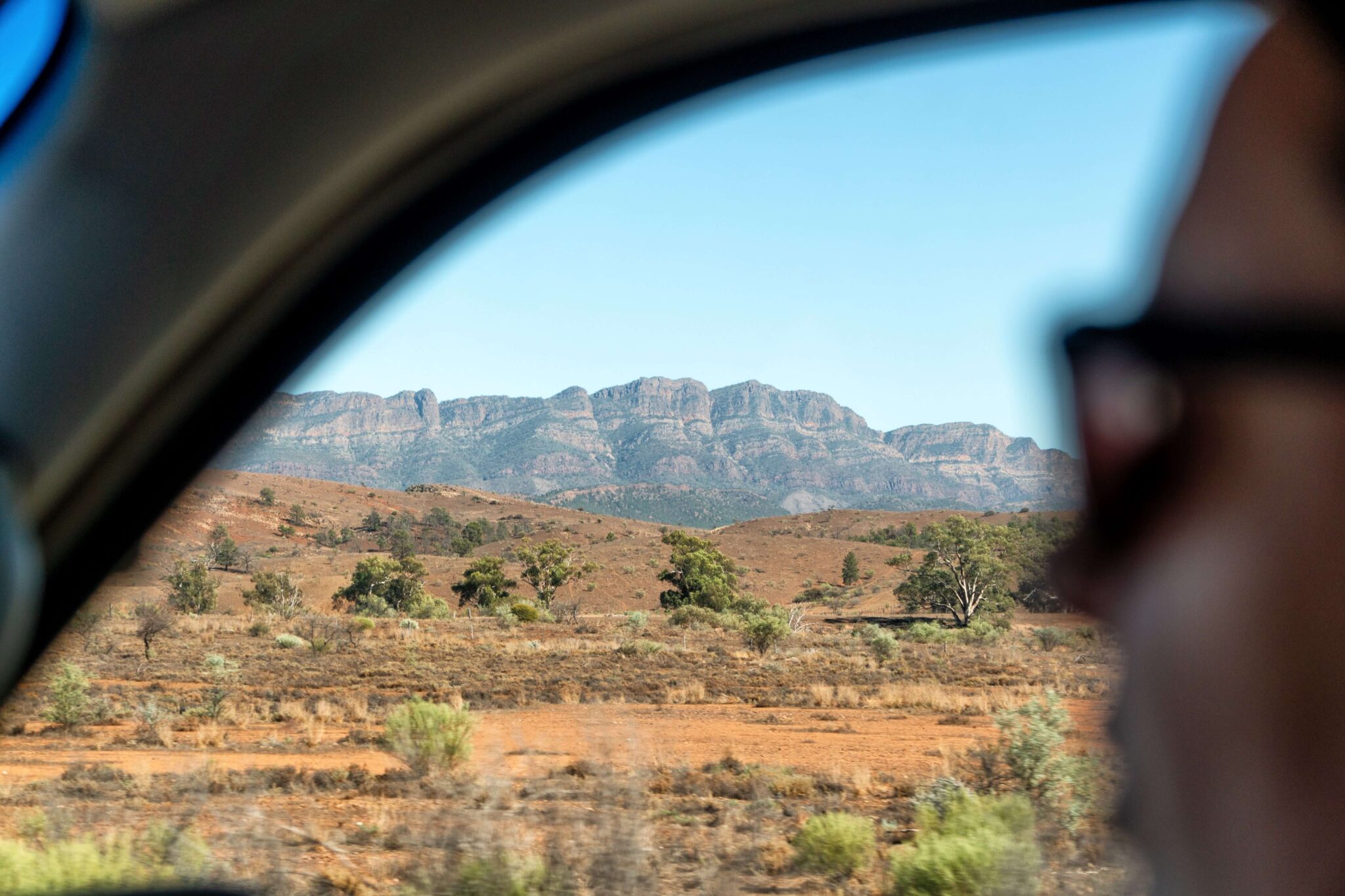 Een backpacker kijkt uit het raam van een camper naar de rotsen van Wilpena Pound.
